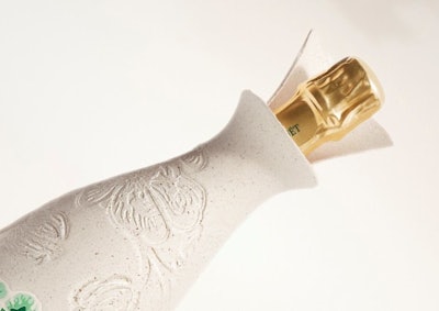 Belle Epoque Cocoon wykazuje organiczny kształt, który delikatnie otacza butelkę. Na górze ujawnia się złota czapka butelki, otoczona kołnierzem przypominającym płatki, formowanego pulp.