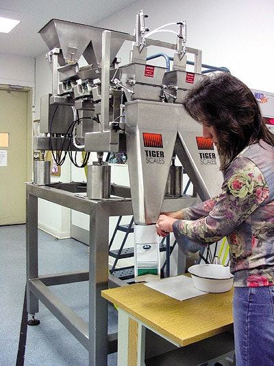 Packaging supervisor Dee Chiodo holds a bag under a funnel for seed filling. By depressing a foot pedal, she releases weighed se
