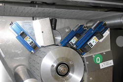 Above photo shows how three TIJ print heads are arranged around one of the cylinders through which lidstock must pass prior to b