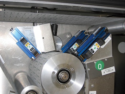 Above photo shows how three TIJ print heads are arranged around one of the cylinders through which lidstock must pass prior to b