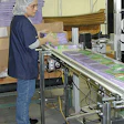 A worker feeds wrapped boxes of chocolates onto a V-belt conveyor for conveying past an ink-jet coder.