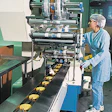 In the foreground (below), a continuous band conveyor feeds cookies by diverters into the infeeds of two parallel wrappers. An o
