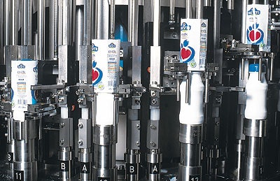 Sealed with foil lids, bottles emerge from the aseptic filling system in two parallel lanes (left). Colorful shrink-sleeve label