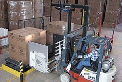 After delivering a load of boxed coolers onto the left side of the shuttle table, a clamp truck driver backs away and pulls a la