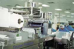 Workers remove packs of surgical gloves from the Tiromat Powerpak (top), a machine equipped with the patented Infrasync drive.
