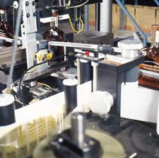 At the first labeling station, a strip stamp label is applied over the top of the bottle (top). Small labels are used to show of