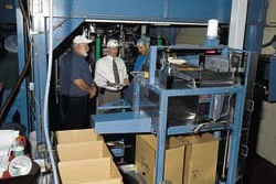 With OR-OSHA and Boyd personnel looking on, erected cases march toward the compact case packer (above). Meanwhile, bags convey f