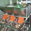 Sausage patties exit the freezer on a conveyor and flow into a pivot pan that feeds patties into a bulk-and-dribble scale (right
