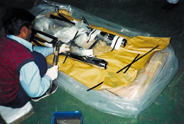 After first covering the pallet with a sheet of corrosion-inhibiting paper, a worker nails down the plastic strips that keep lar