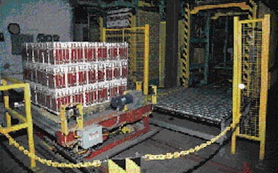 The palletizer offloads the full pallet onto the automated transfer car (left), which moves on tracks embedded in the floor. The