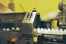 A worker at right adds bottles to a floor-level hopper that feeds them into the new bottle unscrambler at the Naturally Vitamins