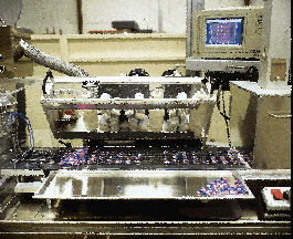 The brush box feeder (far left), shown lifted off the web, uses a series of brushes to distribute tablets into cavities. Interna