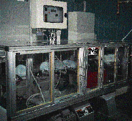 A group of mechanical fingers (shown at bottom left in the photo at left) remove six blow-molded 1-gal HDPE jugs and place them