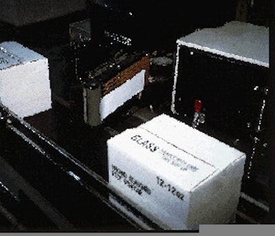 A printed label held by a vacuum grid awaits an oncoming case (right). After the front portion is applied, the side is brushed d