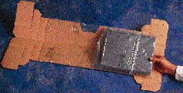 The flat blank is folded in half down the center, loosening the plastic sleeve enough to permit the computer to be tucked inside