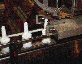 Cap feeder delivers caps to capper, which has a removable brass chute end (inset) dedicated to each cap size. No tools are neede