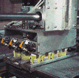 Reciprocating pickup head mechanically grips a case load of cups (left) and delivers them to a waiting case blank (above