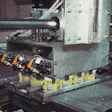 Reciprocating pickup head mechanically grips a case load of cups (left) and delivers them to a waiting case blank (above