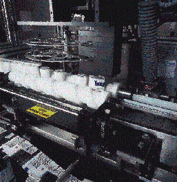 After filling, printed rollstock is perforated, cut and guided over the container before it enters the shrink tunnel. Perfecting