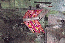 The laser-coded roll of printed material unwinds (from left to right) into the first station within the flow wrapper for sealing