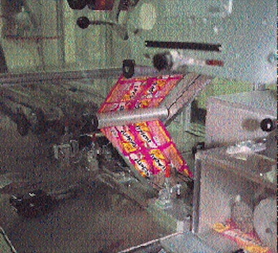 The laser-coded roll of printed material unwinds (from left to right) into the first station within the flow wrapper for sealing
