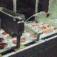 Lidded trays exit the vacuum sealing chamber (upper right) and move through two perforating stations followed by two cross-cutti