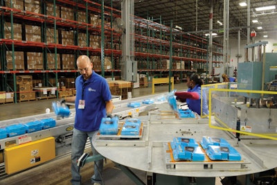 CLOSING OPERATION. Station workers at ATC Logistics & Electronics seal clamshells protecting the GPS cartons.