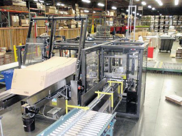 MAGAZINE FEED. Photo above shows knocked-down corrugated cases stacked in a magazine feed on the left and product infeed on the