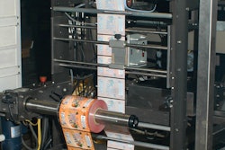 A roll of preprinted film, supplied by the customer, unwinds at the foot of the vertical form/fill/seal machine, then feeds upward for bag filling and sealing.