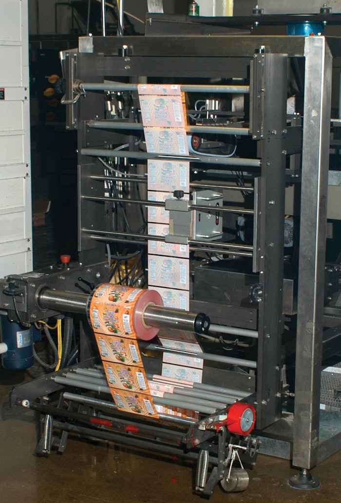 A roll of preprinted film, supplied by the customer, unwinds at the foot of the vertical form/fill/seal machine, then feeds upward for bag filling and sealing.