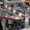 BOTTLE TRACKER. As bottles travel up to the BottleTracker by conveyor, an outsert machine applies a topsert on top of the bottles. This is a folded leaflet applied to the top of each bottle that contains information related to the product.