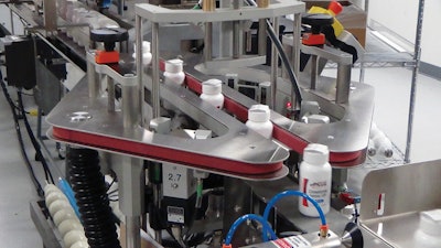 BOTTLE TRACKER. As bottles travel up to the BottleTracker by conveyor, an outsert machine applies a topsert on top of the bottles. This is a folded leaflet applied to the top of each bottle that contains information related to the product.