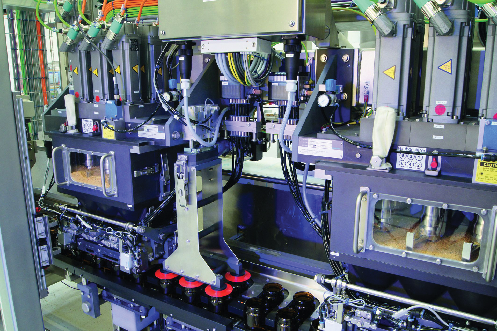 SIX PRE-DOSERS. The customized modular linear filler features a portioning system that begins with six pre-dosers that fill containers approximately 80% of the fill volume using a large auger filler.