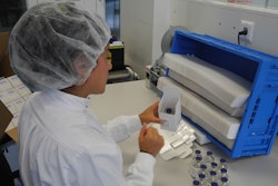 MANUAL PACKING. An operator places a glass vial into the clinical trials carton.