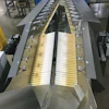 Shown here is one of 12 automated feeding systems. Including both left and right sides, each feeding system deploys 180 rollers in clusters of six. Each cluster has its own sensor, its own stepper motor/drive combo, and its own controller. Because each cluster communicates with the ones around it, each controller knows if the overall goal of singulating the flow of pouches will be better accomplished by speeding up or slowing down its six rollers.