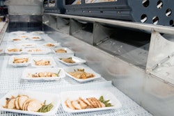 A fresh batch of vacuum skin-packed trays that have just exited the HPP vessel are conveyed toward labeling and secondary packaging.