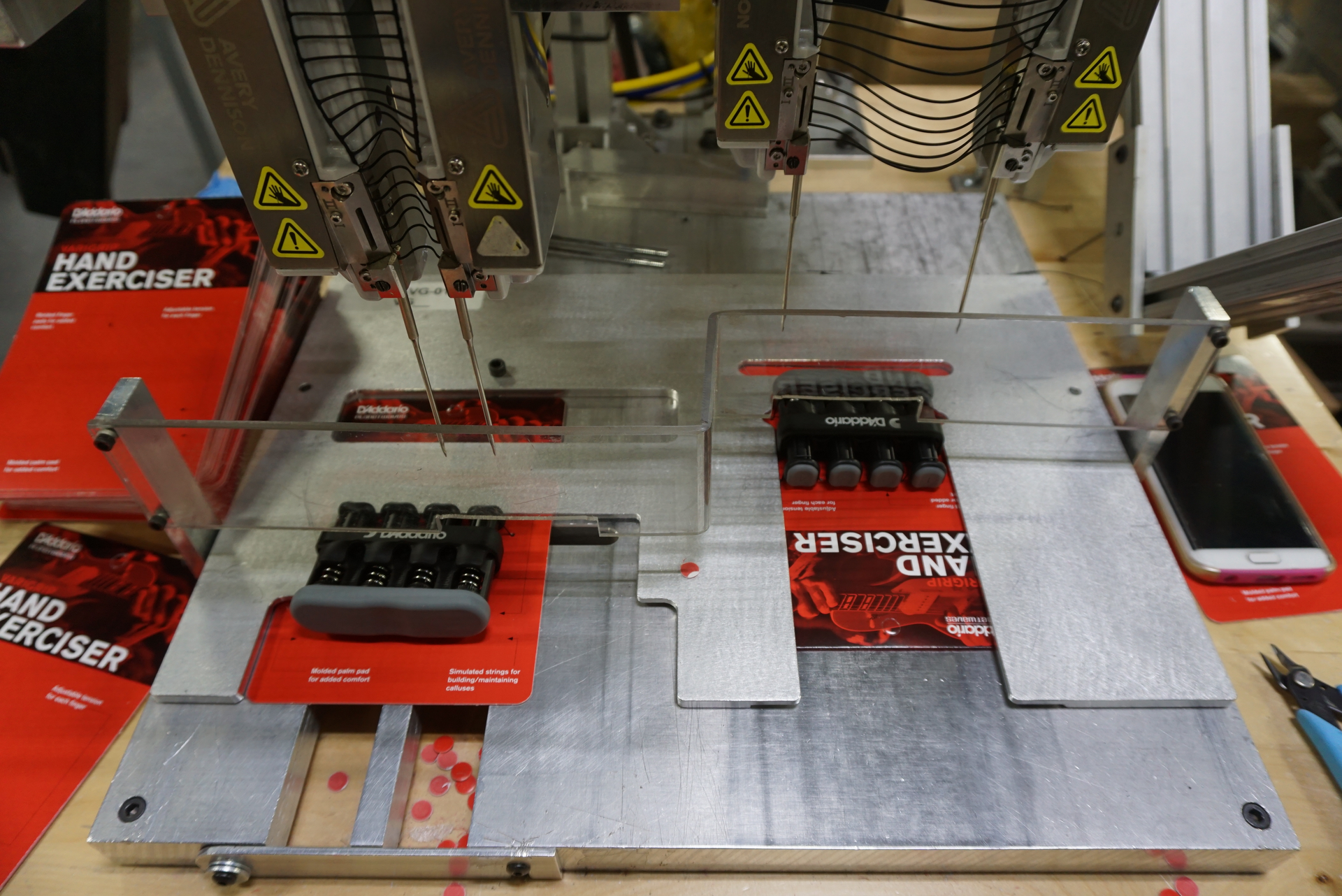 A black elastic staple is applied to a backing card to hold a hand exerciser in place.