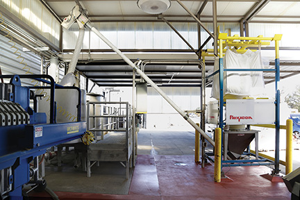 Diatomaceous earth moves froth bulk bag through the hopper, flexible screw conveyor and downspout to a 300 gal. before filtration of the wine. The enclosed system eliminates dust and reduces costs from manual dumping of bags. Photo courtesy of Flexicon