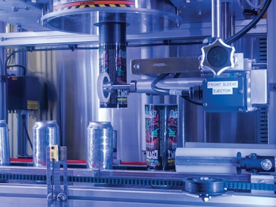 Closeup of labeler shows one can with a freshly cut label that has just been applied while the next can waits for application of its label.