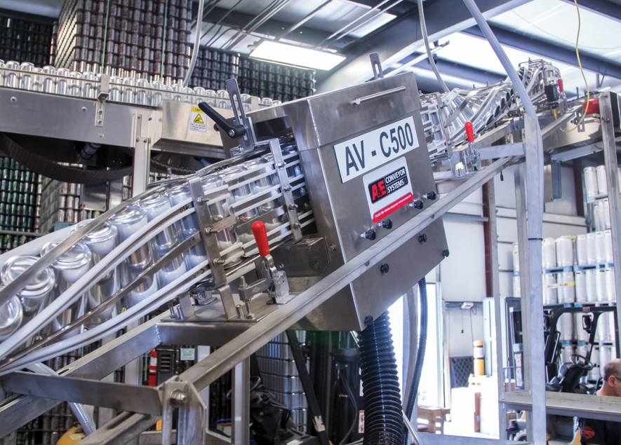 Closeup of labeler shows one can with a freshly cut label that has just been applied while the next can waits for application of its label.