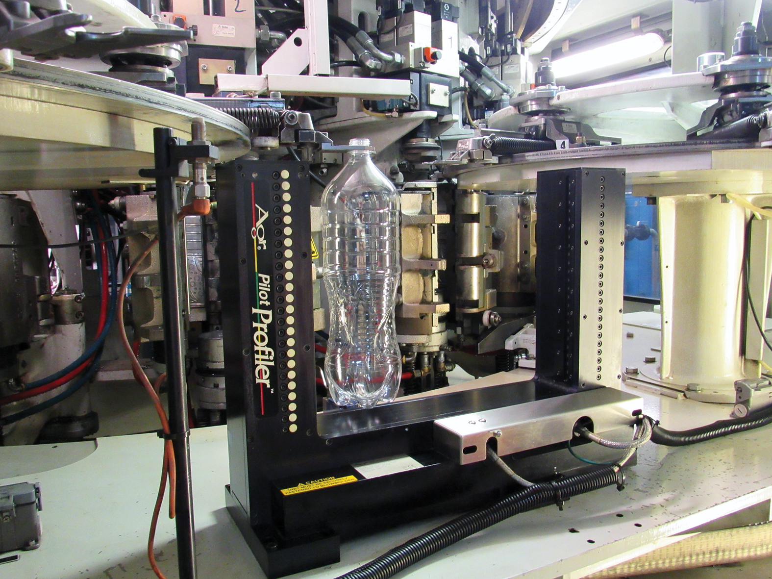 The Process Pilot goalpost sits in the blowmolder takeout area, its sensors measuring bottle thickness at 12.5-mm intervals along the sidewall.