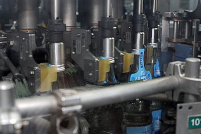 Close-up of the Innoket Neo labeler shows the shoulder-label seal being applied to the bottles.