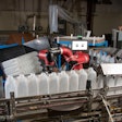 The cobot stacks bottles into a bin, replacing three operators over three shifts.