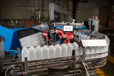 The cobot stacks bottles into a bin, replacing three operators over three shifts.