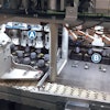 Closure Subassemblies—each in a puck and each already filled with liquid amplifier—enter the Nuspark system and are immediately pushed from a white conveyor belt and into a station where four mechanical grippers (A in photo) orient them four at a time. The pucks are then pushed to the next position (B in photo), where four Casing Subassemblies come down from above and are placed in the four Closure Subassemblies. Then the four pucks are pushed back onto the white conveyor belt, which takes them to the next station.