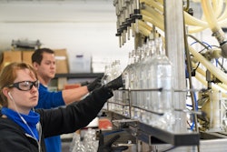 Skye Clarke (front) and Sam Epperson (back) of Cardinal Spirits fill bottles of hand sanitizer that are headed to a senior living community.