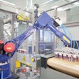 This robot picks freshly printed cans six at a time from the vacuum conveyor discharge and places them on the infeed conveyor of the curing oven.
