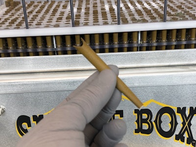 Filled pre-rolls are removed from the lower cartridge for weighing, folding closed, and manual packing.