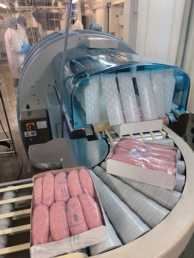Freshly wrapped paperboard trays of fresh sausages emerge from the cling film application system.