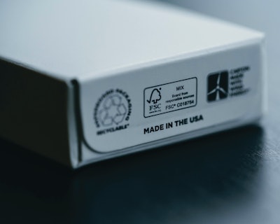 Beneath the cartons are logos and icons communicating the paperboard is a recyclable material, produced using wind power, with FSC certifications.